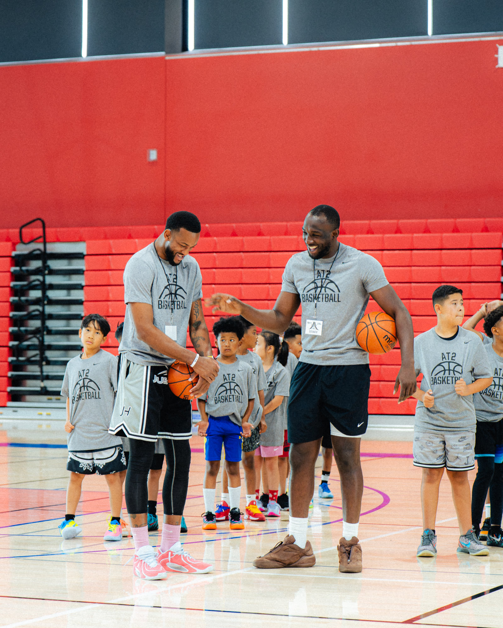 Pro athletes sharing a laugh with young campers lined up on court at AT2